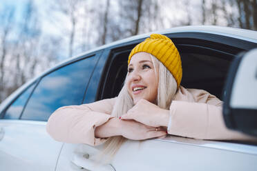 Happy woman leaning out of car window in winter forest - OLRF00117