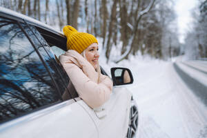 Frau mit Strickmütze, die sich im Winterwald aus dem Autofenster lehnt - OLRF00120