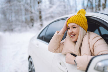 Happy woman with head in hand leaning out of car window in forest - OLRF00121