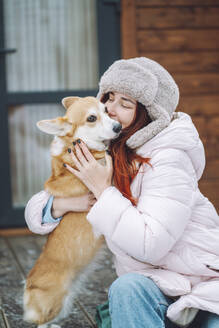 Young woman kissing Corgi dog on porch - OLRF00132