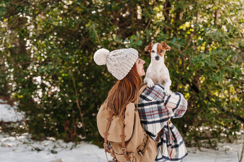 Glückliche Frau mit Rucksack und Hund in der Nähe eines Baumes - EBBF08293