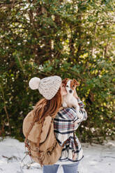 Woman wearing knit hat and kissing dog in winter - EBBF08294