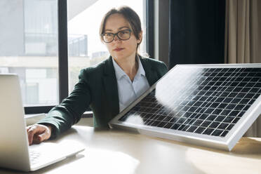 Engineer showing solar panel on video call through laptop in office - OSF02359