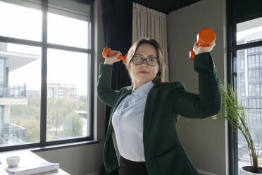 Businesswoman wearing eyeglasses and exercising with dumbbell at office - OSF02365