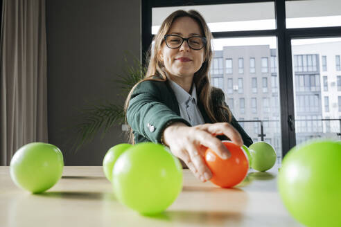 Smiling businesswoman reaching for red ball kept on desk in office - OSF02369