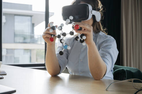 Wissenschaftler, der ein Virtual-Reality-Headset trägt und eine Molekularstruktur am Schreibtisch hält - OSF02373