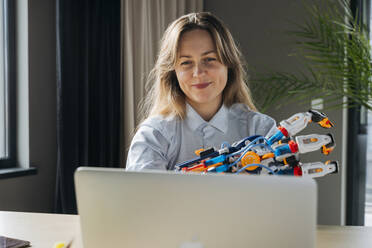 Smiling engineer showing robot arm project on video call through laptop in office - OSF02375