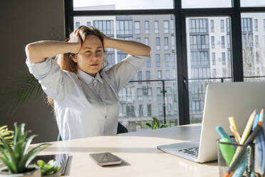 Müde Geschäftsfrau mit Kopf in den Händen sitzt am Schreibtisch im Büro - OSF02376