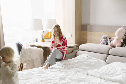 Smiling girl sitting near bed at home - SEAF02173