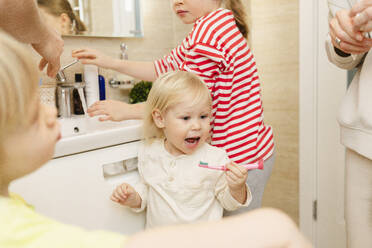 Girl brushing teeth with family in bathroom at home - SEAF02183