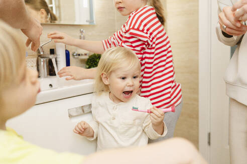 Mädchen beim Zähneputzen mit Familie im Badezimmer zu Hause - SEAF02183