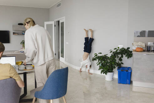 Junge macht Handstand an der Wand, während die Mutter zu Hause arbeitet - SEAF02190