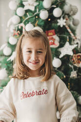 Lächelndes Mädchen vor einem Weihnachtsbaum zu Hause - EBBF08311