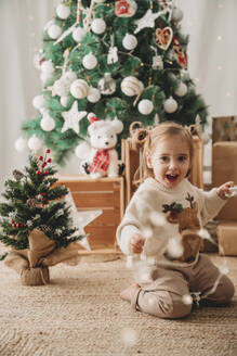 Glückliches Mädchen spielt in der Nähe von Weihnachtsbäumen zu Hause - EBBF08326