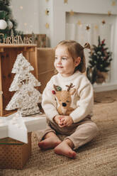 Lächelndes Mädchen sitzt in der Nähe von Weihnachtsdekoration zu Hause - EBBF08331