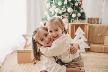 Mädchen umarmt Schwester im Wohnzimmer zu Hause - EBBF08334