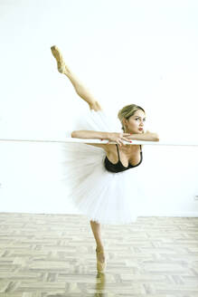 Ballerina stretching leg near barre in studio - YHF00097