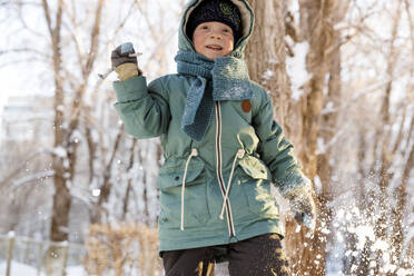 Smiling boy throwing stick in snow - MBLF00252