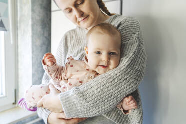 Lächelndes süßes Baby in den Armen der Mutter zu Hause - IHF01874