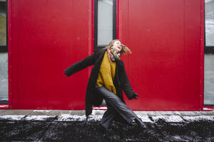 Glückliche junge Frau tanzt vor einer roten Wand - EYAF02945