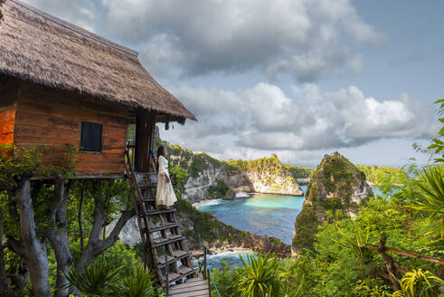 Schönes Mädchen mit weißem Kleid steht auf der Spitze des Baumhauses mit Blick auf die Aussicht auf Diamond Beach, Nusa Penida, Klungkung Regentschaft, Bali, Indonesien, Südostasien, Asien - RHPLF31680