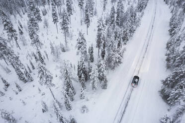 Luftaufnahme eines Autos, das durch den schneebedeckten Wald auf einer vereisten Straße fährt, Akaslompolo, Finnisch-Lappland, Finnland, Skandinavien, Europa - RHPLF31918