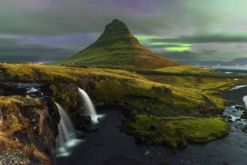 Der Berg Kirkjufell und der Wasserfall Kirkjufellfoss mit verblasstem Nordlicht (Aurora Borealis) hinter Wolken, Snaefellsnes-Halbinsel, Westisland, Island, Polarregionen - RHPLF31922