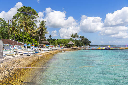 Blick auf einen tropischen Strand mit Palmen und Bäumen entlang der Küste der Insel Nusa Penida, mit traditionellen indonesischen Holzbooten (jukung) (kano) (cadik), am Strand, Insel Nusa Penida, Regentschaft Klungkung, Bali, Indonesien, Südostasien, Asien - RHPLF31925