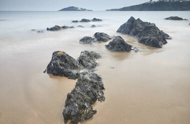 In Sand eingegrabene Felsbrocken an der Küste in der Abenddämmerung, Blick vom Strand von Bantham auf Burgh Island an der Südküste von Devon, England, Vereinigtes Königreich, Europa - RHPLF32133