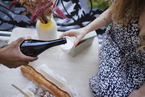 Hand eines Mannes gießt Wein in ein Glas für eine Frau auf dem Balkon - DANF00006