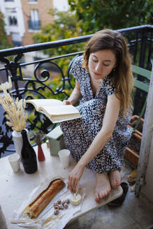Frau hält Buch und isst auf dem Balkon - DANF00024