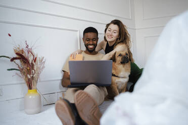 Smiling freelancers using laptop near dog at home - DANF00038