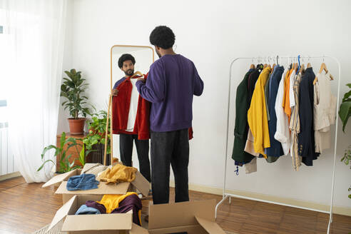 Young man examining and decluttering clothes at home - VRAF00270