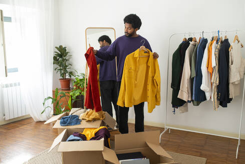 Young man organizing and decluttering clothes at home - VRAF00271