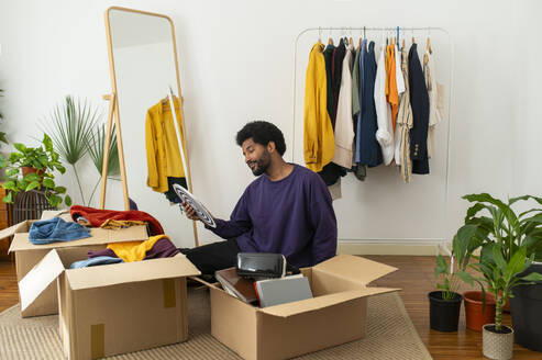 Young man decluttering clothes and objects at home - VRAF00275