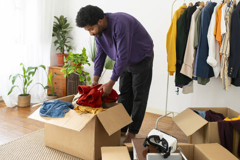 Young man doing decluttering of clothes at home - VRAF00277