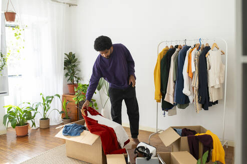 Man organizing and decluttering clothes in cardboard boxes - VRAF00279