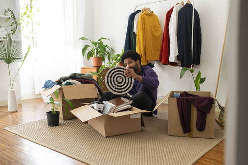 Young man organizing clothes and objects in cardboard boxes - VRAF00284