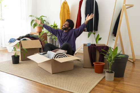 Cheerful young man with arms raised organizing and decluttering at home - VRAF00285