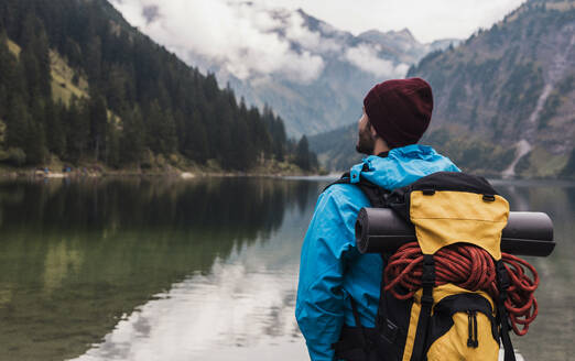 Man with backpack standing in front of lake Vilsalpsee and mountains at Tyrol, Austria - UUF31084