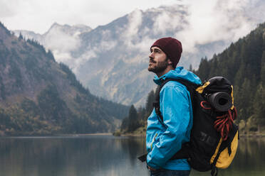 Young man with backpack standing in front of lake Vilsalpsee and mountains at Tyrol, Austria - UUF31085