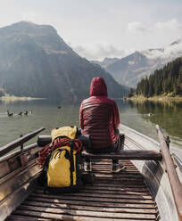 Junge Frau mit Rucksack im Boot sitzend auf dem Vilsalpsee in der Nähe der Berge, Tirol, Österreich - UUF31087