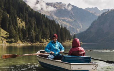 Young couple riding in boat at lake Vilsalpsee near mountains, Tyrol, Austria - UUF31088