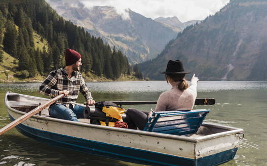 Junge Frau gestikuliert mit einem Mann, der in einem Boot am Vilsalpsee in der Nähe der Berge sitzt, Tirol, Österreich - UUF31091