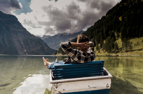 Young man sitting in boat at lake Vilsalpsee near mountains, Tyrol, Austria - UUF31092