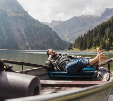 Young man relaxing in boat at lake Vilsalpsee near mountains, Tyrol, Austria - UUF31093