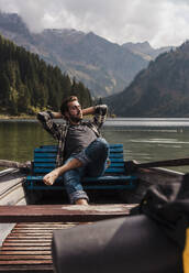 Young man relaxing in boat at lake Vilsalpsee near mountains on sunny day, Tyrol, Austria - UUF31094
