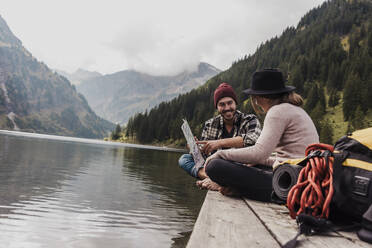 Happy young couple sitting with map on pier near lake Vilsalpsee and mountains at Tyrol, Austria - UUF31098