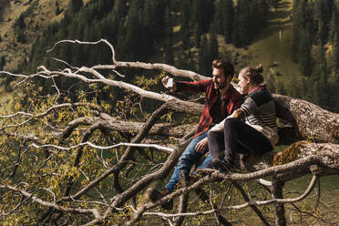 Pärchen macht Selfie mit Smartphone auf umgestürztem Baumstamm in der Nähe des Vilsalpsees in Tirol, Österreich - UUF31107