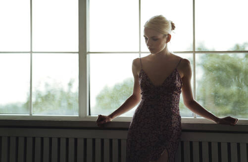 Nachdenkliche junge Frau steht am Fenster zu Hause - AZF00597